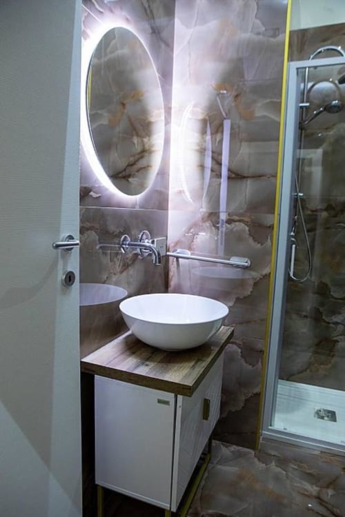 Bagno moderno a Dreams & Colors Napoli con lavabo bianco a coppa, specchio ovale illuminato e pareti in marmo
