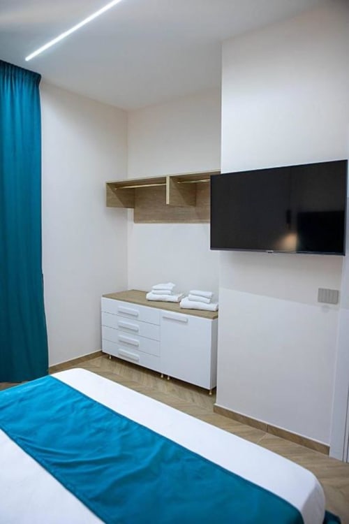 Camera tripla moderna presso Dreams & Colors B&B a Napoli con dettagli blu, TV a schermo piatto, mobili bianchi e finiture in legno