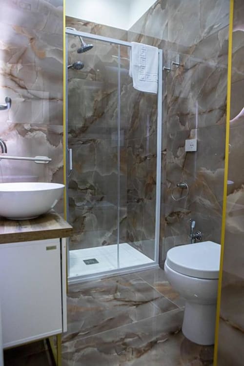 Bagno moderno al Dreams & Colors B&B di Napoli con pareti in marmo, box doccia in vetro, lavabo e wc bianchi
