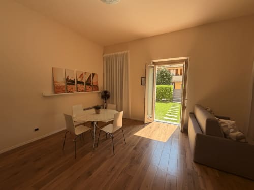 Bright apartment at DV Garda Suite with dining table, sofa, wooden floors, and garden view through glass doors