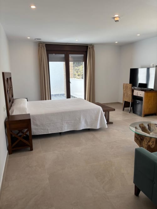 Spacious junior suite with river views at Hotel Mulhacén Trevélez, featuring a bed, TV, and terrace access in Granada.