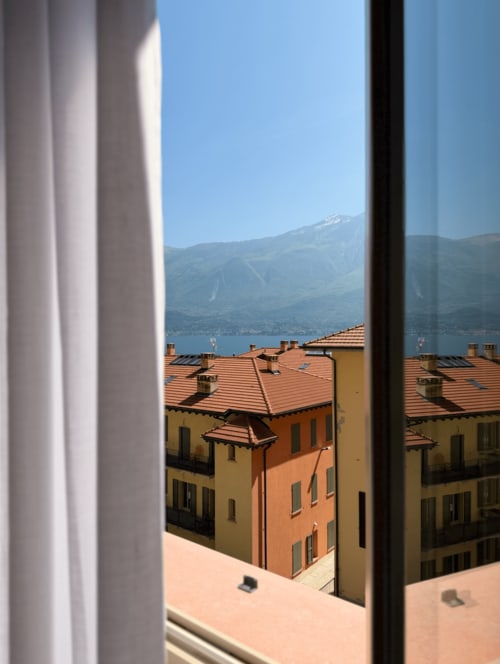 View from DV Garda Suite apartment in Campione showing terracotta-roofed buildings, lake, and snow-capped mountains