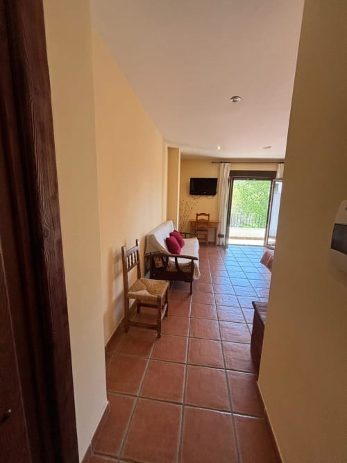 Pasillo de la Junior Suite del Hotel Mulhacén Trevélez con baldosas de barro, puerta de madera, silla y vista hacia la sala de estar