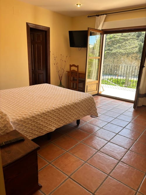 Spacious bedroom with terrace at Hotel Mulhacén Trevélez, featuring bed, TV, wooden furnishings, and river valley views from