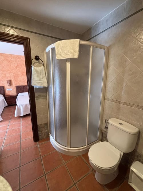 Baño con cabina de ducha, inodoro y alicatado en tonos beige del Hotel Mulhacén Trevélez