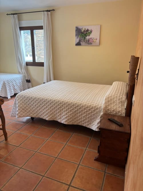 Bright bedroom in Hotel Mulhacén Trevélez with wooden bed, cream bedding, terracotta tile floor, and mountain views through