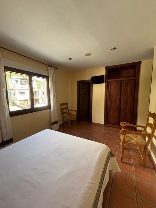 Spacious double room at Hotel Mulhacén Trevélez with bed, wooden wardrobe, terracotta flooring and mountain views from window
