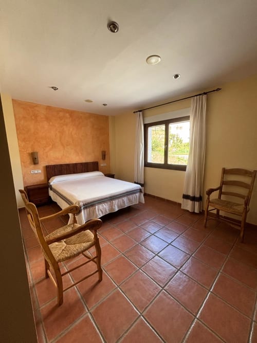 Double bedroom at Hotel Mulhacén Trevélez with terracotta tile floor, orange accent wall, wooden furniture and garden views