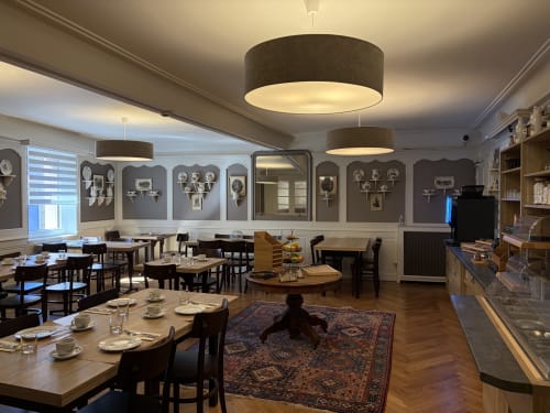 Élégante salle à manger de l'Hôtel de l'Ange à Niedermorschwihr avec luminaires suspendus, présentoirs muraux sombres et tables dressées.