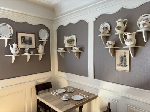Élégante salle à manger de l'Hôtel de l'Ange aux murs gris et blanc, étagères décoratives exposant de la porcelaine vintage et un