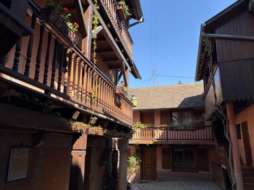 La cour pittoresque de l'Hôtel de l'Ange à Niedermorschwihr avec son architecture à colombages et ses fleurs suspendues.