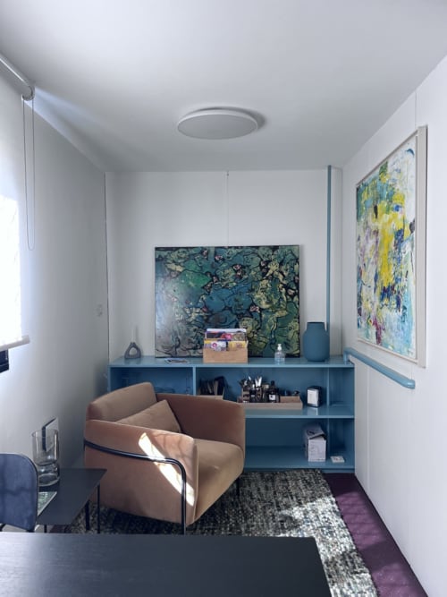 Estudio moderno en La Porte Rouge en Roubaix con sillón beige, estanterías azules y cuadros enmarcados en paredes blancas
