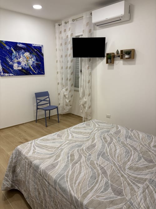 Modern apartment bedroom at Catalogna10 Rooms, Alghero, with bed, TV, AC unit, and blue chair