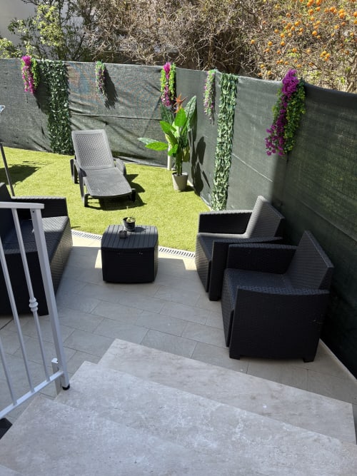 Modern outdoor patio at Catalogna10 in Alghero with black rattan seating, gray privacy screens, purple flowering plants, and