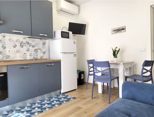 Modern apartment kitchen and dining area at Catalogna10 in Alghero with blue cabinetry, dining table, and living space