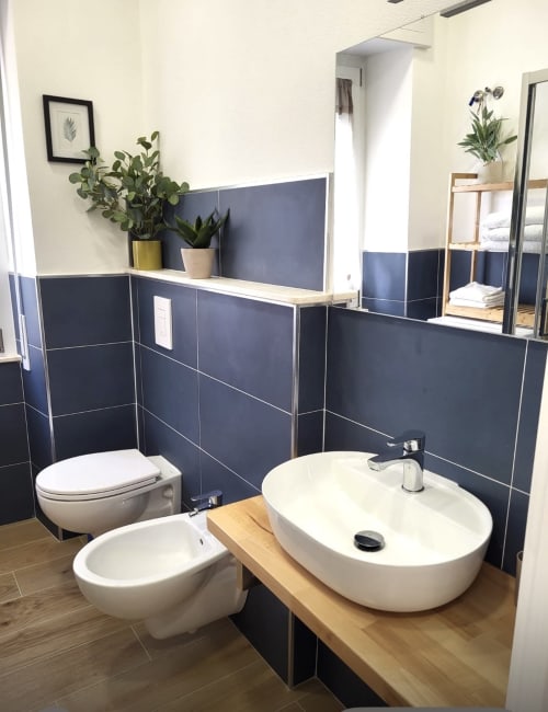 Modern bathroom at Catalogna10 hotel in Alghero with white vessel sink, toilet, dark blue tile walls, and wooden counter
