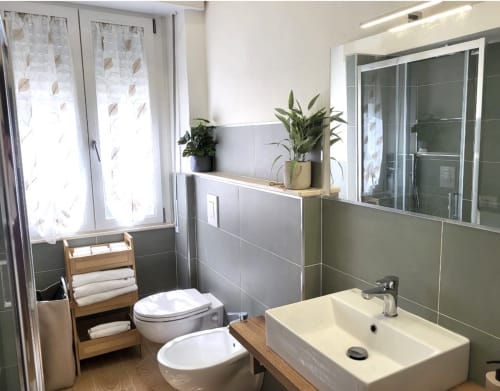 Modern bathroom at Catalogna10 Rooms in Alghero with white sink, toilet, green tile walls, wooden shelving, potted plants,