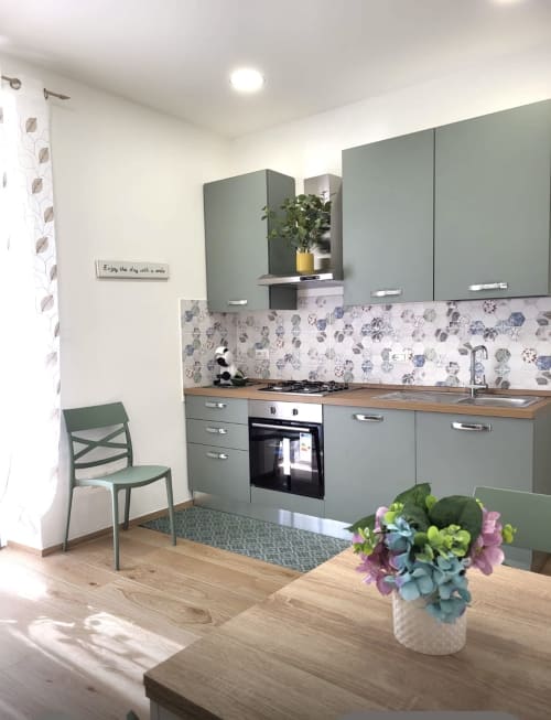 Modern kitchen apartment at Catalogna10 Rooms, Alghero with sage green cabinets, floral backsplash, and dining area