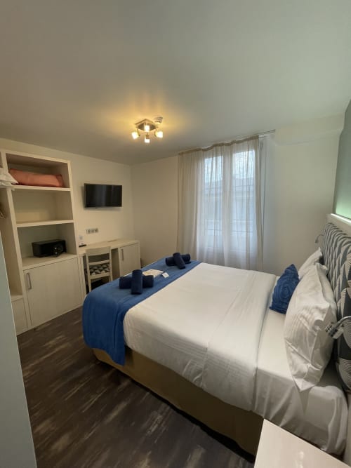 Standard double room with sea view at Hotel Flots d'Azur in Nice, featuring white bedding, blue accents, TV, and modern