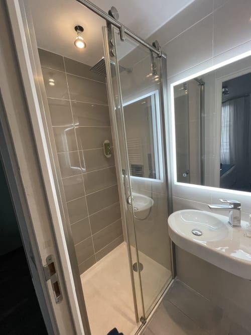 Modern bathroom with glass shower enclosure, illuminated mirror, white sink, and beige tile walls at Hotel Flots d'Azur Nice