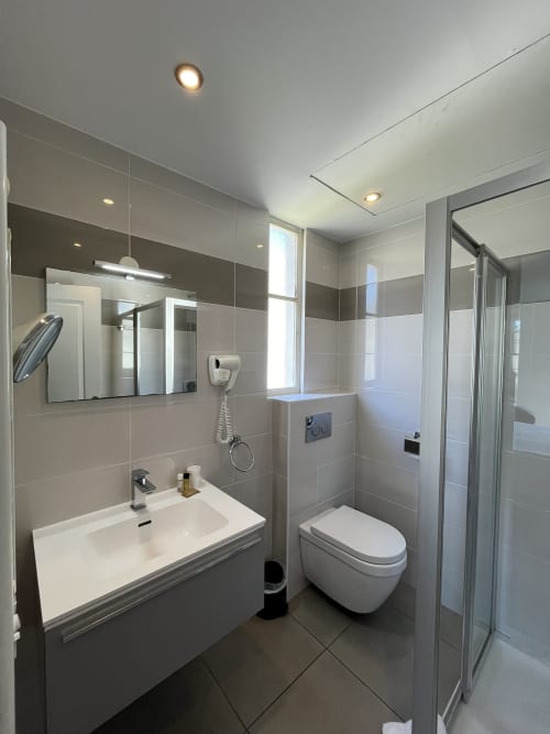 Modern bathroom at Hotel Flots d'Azur Nice with white sink, wall mirror, toilet, and shower enclosure