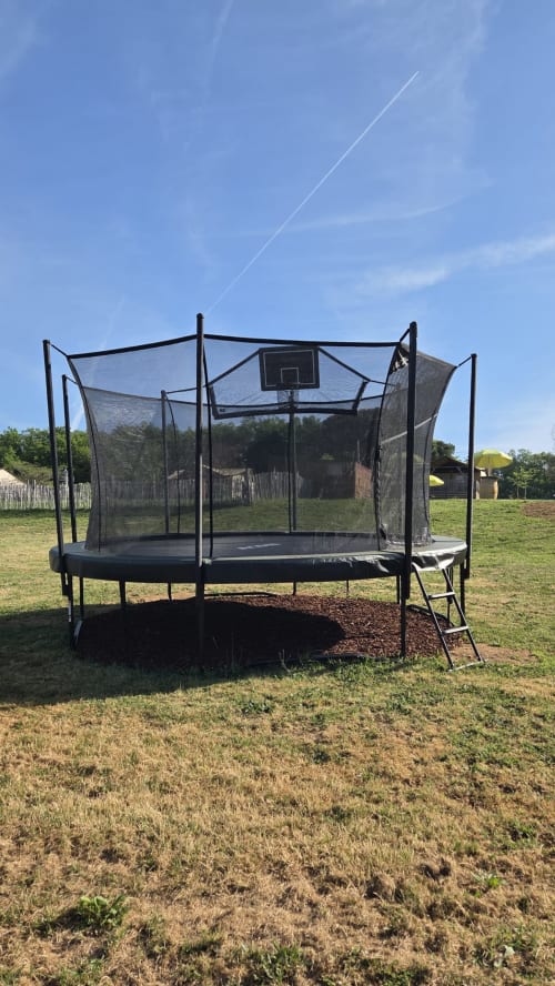 Trampoline noir avec panier de basket et filet de sécurité dans un champ herbeux à Home Sweet Lodge Glamping Aquitaine