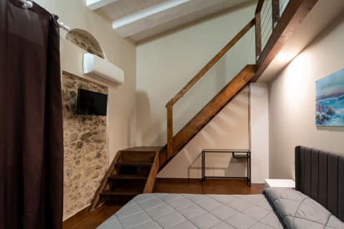 Camera da letto in cottage di pietra con scala in legno, letto e vista sul giardino a Novi Velia