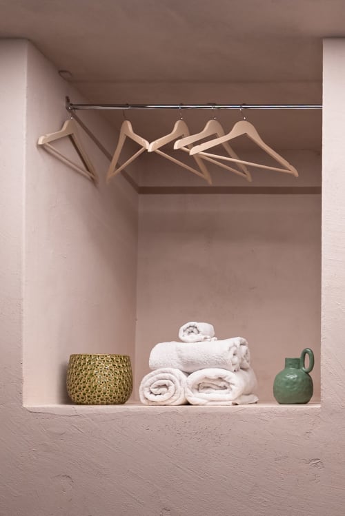 Scaffale minimalista del bagno a Stone House Gebel el Son con appendini in legno, asciugamani bianchi arrotolati, cesto intrecciato e verde