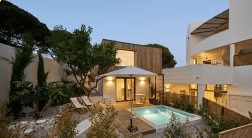 Casa Redonda Duplex with private pool, lounge chairs, wooden deck, and illuminated interior at dusk in Portugal