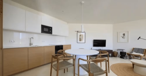 Modern open-plan apartment at Casa Redonda Aroeira with white kitchen, wooden dining table, and living area with TV