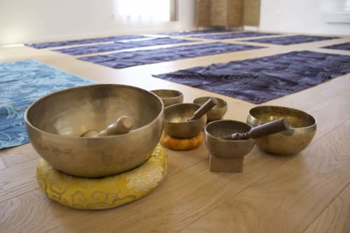 Singing bowls and strikers arranged on wooden floor at Espace Ker Gana wellness space in Plourin