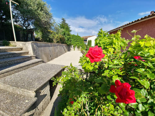 Cour ensoleillée de l'hôtel Smooth Luberon à Villars avec roses rouges, allées en pierre et architecture provençale traditionnelle