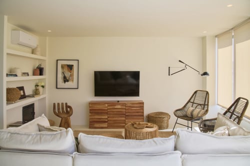 Modern apartment living room at Casa Redonda Aroeira with white sofa, wooden media console, rattan chairs, and wall-mounted