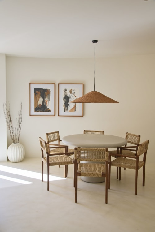 Modern dining room at Casa Redonda Aroeira with round table, woven chairs, pendant light, and abstract art.