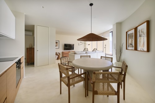 Open-plan apartment at Casa Redonda Aroeira with dining area, round table, woven chairs, kitchen, and pool view in Portugal