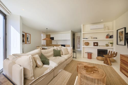 Modern apartment at Casa Redonda Aroeira with cream sofa, wooden accents, white shelving, and pool view from windows.
