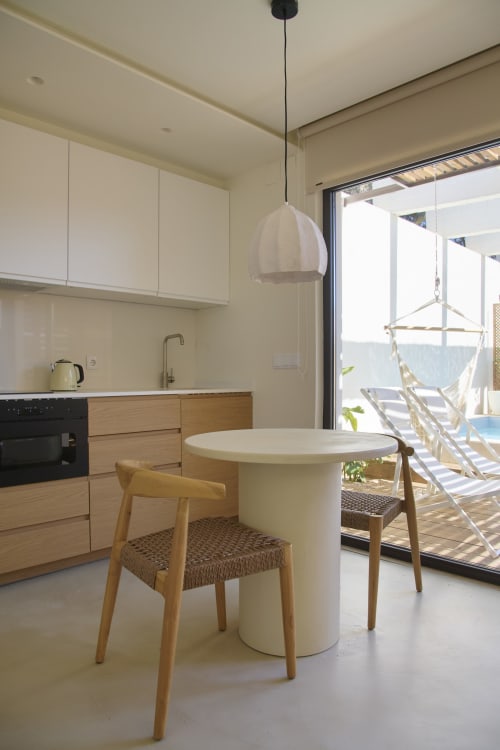 Cozinha moderna em estúdio com mesa redonda branca, cadeiras de madeira e vista para a piscina na Casa Redonda Aroeira, Portugal