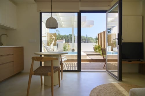 Estúdio na Casa Redonda Aroeira com vista para piscina, mesa de jantar, luminária pendente e portas de terraço abertas