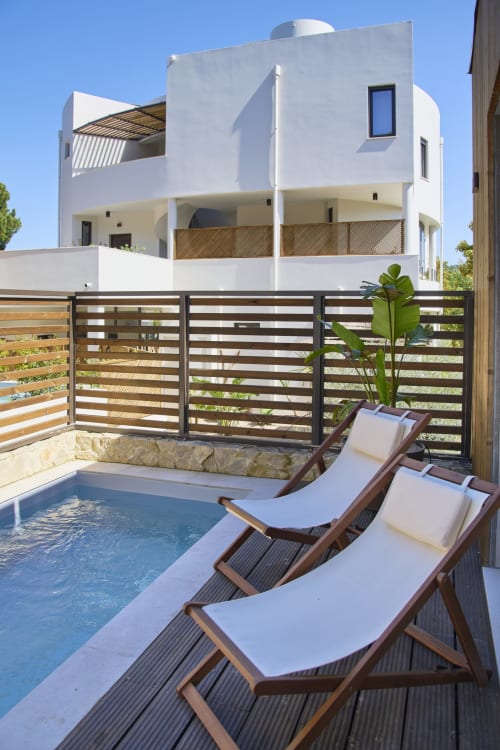 Modern white bungalow with pool, lounge chairs, and wooden gate at Casa Redonda Aroeira, Portugal