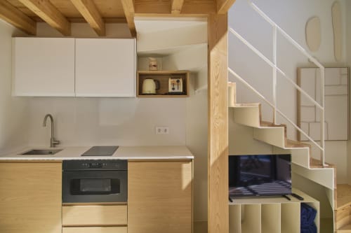 Modern compact kitchen with wood cabinetry, white countertops, and black oven in Casa Redonda Duplex apartment, Portugal