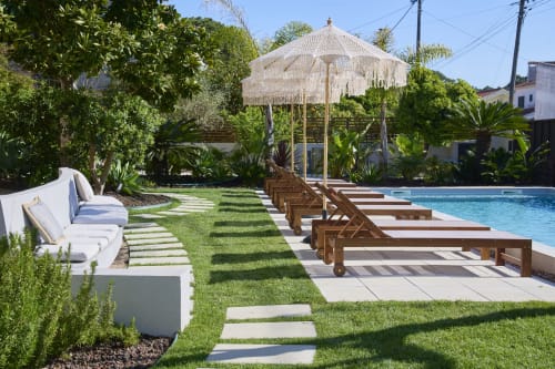Luxurious poolside lounge at Casa Redonda Aroeira villa in Portugal with wooden loungers, thatched umbrella, and manicured