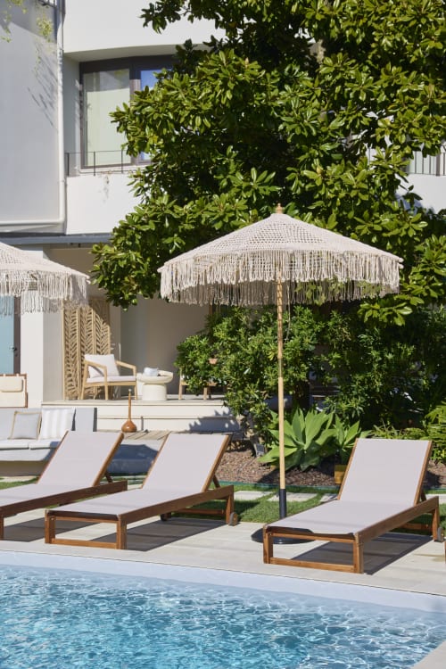 Luxury pool lounge at Casa Redonda Aroeira villa with wooden sunbeds, fringed umbrella, and lush greenery