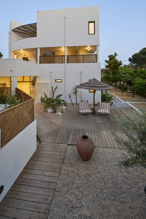 Modern white villa courtyard at Casa Redonda Aroeira with wooden deck, lounge chairs, and umbrella in Portugal