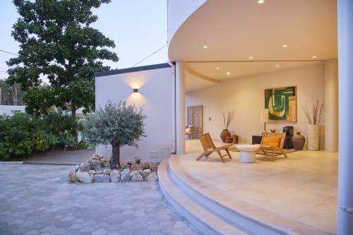 Casa Redonda Aroeira villa courtyard with curved modern interior, olive tree, and lounge seating at dusk