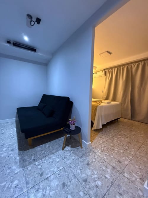 Suíte moderna no Downtown Rooftop 375 em Macaé com cadeira preta, mesa lateral e quarto com cortinas