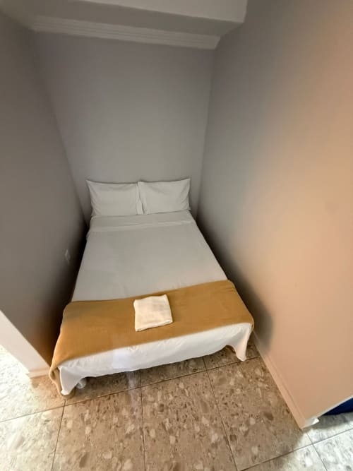 Quarto de hotel compacto no Downtown Rooftop 375 em Macaé com roupa de cama branca, banco de madeira e piso em azulejo