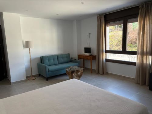 Modern hotel room at Hotel Mulhacén Trevélez with bed, blue sofa, desk, and mountain views through large windows