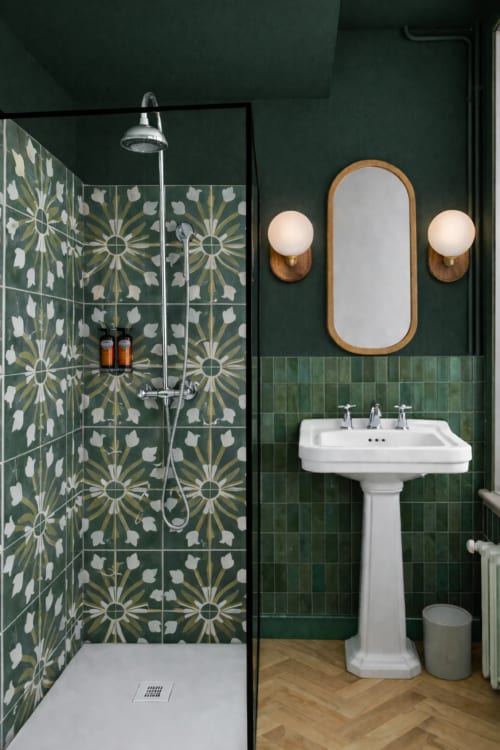 Salle de bains élégante aux carreaux verts à La Maison 1903, avec lavabo sur piédestal, miroir orné et paroi de douche à motifs