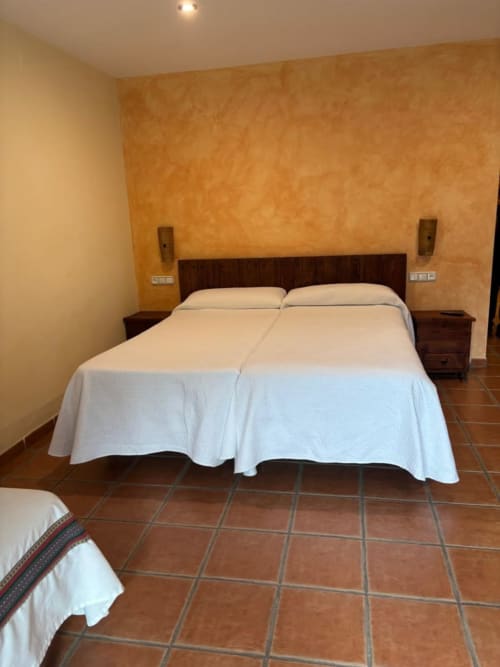Modern hotel bedroom at Hotel Mulhacén Trevélez with double bed, white linens, dark wood headboard, and terracotta tile