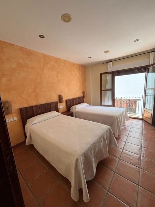 Twin bedroom with terracotta floor and orange accent wall at Hotel Mulhacén Trevélez, Granada